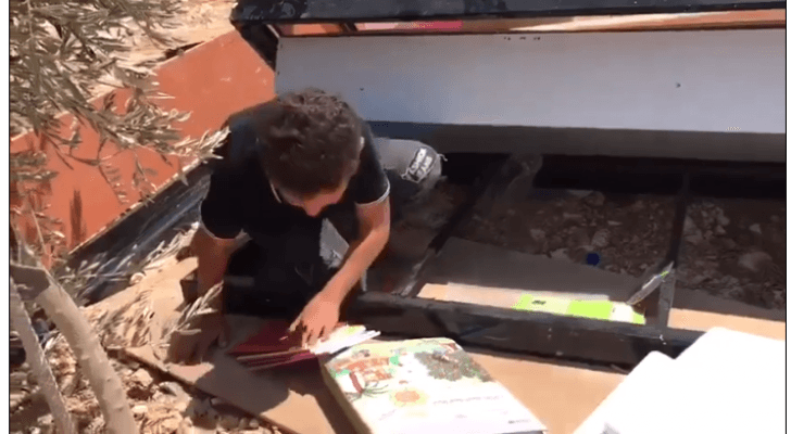 طفل فلسطيني يجمع كتبه من بين ركام منزل عائلته الذي هدمه جيش الاحتلال