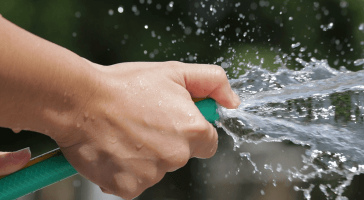 صورة تعبيرية لشخص يستخدم خرطوم مياه