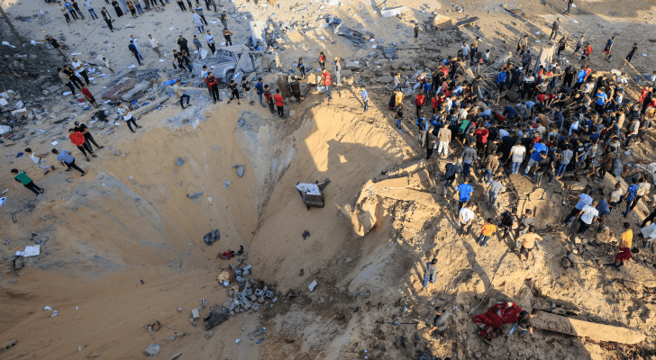 فلسطينيون يقفون بجوار حفرة ناجمة عن انفجار ضربة جوية في خان يونس جنوب قطاع غزة