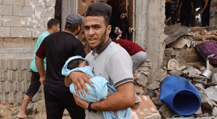 فلسطيني يحمل طفلة بعد قصف الاحتلال الإسرائيلي لمنزله في قطاع غزة