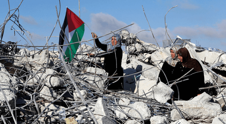 فلسطينية تحمل علم فلسطين فوق الركام
