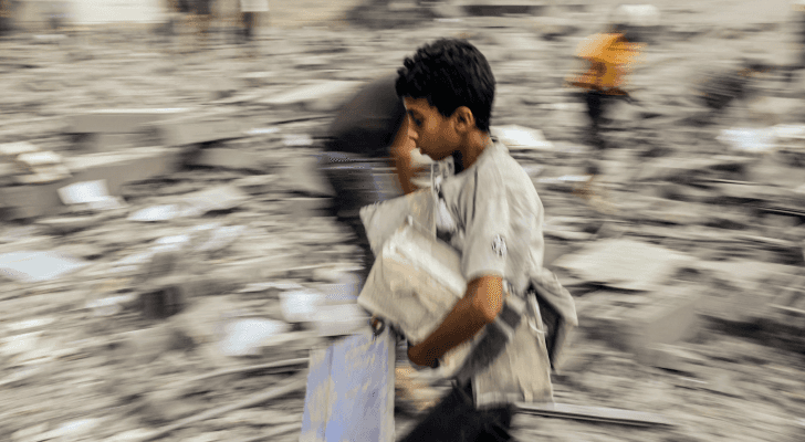 طفل من غزة يحمل كتب ويركض هربا من قصف الاحتلال