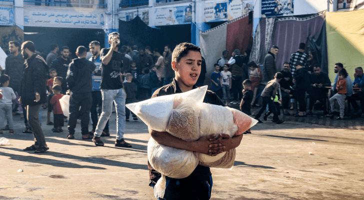 فتى فلسطيني يسير بأكياس من الإمدادات الغذائية في مدرسة تديرها "الأونروا" بقطاع غزة