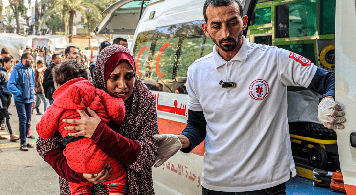 فلسطينية تحمل طفل مصاب جراء قصف الاحتلال على قطاع غزة