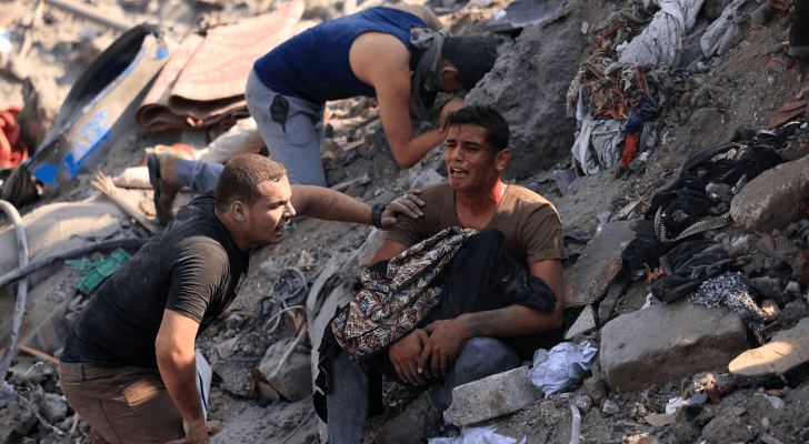 فلسطينيون يجلسون على أنقاض أحد المنازل الذي دمرته غارات للاحتلال الإسرائيلي في قطاع غزة