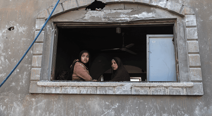 فلسطينيتان تتأملان من نافذة أحد المنازل الذي تعرض للقصف في غارة جوية للاحتلال في خان يونس