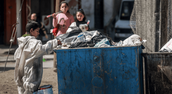 طفل فلسطيني يبحث في سلة نفايات عن طعام أو شي يستفيد منه