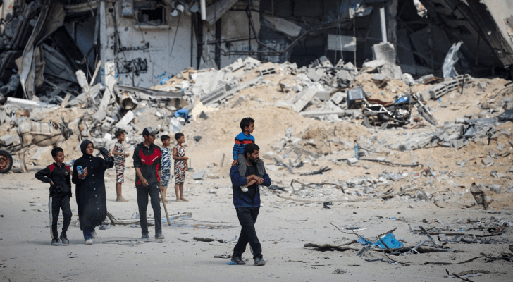 أشخاص يسيرون بجوار أنقاض المباني التي دمرت خلال قصف الاحتلال في خان يونس