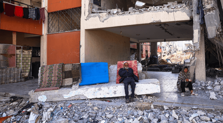 فلسطينيون يجلسون أمام مبنى منزلهم الذي دمره الاحتلال في خان يونس بجنوب قطاع غزة
