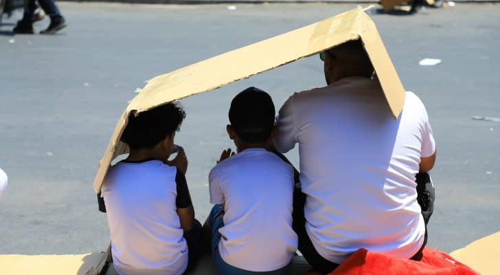 شخص وفتيان يستظلون بـ"كرتونة" من أشعة الشمس