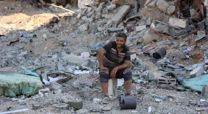 فلسطيني يجلس على ركام منزله ويبتسم رغم الجراح في غزة