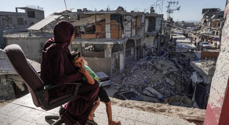 سيدة فلسطينية تجلس مع ابنها على شرفة منزلها الذي دمر بعدوان الاحتلال جنوب غزة