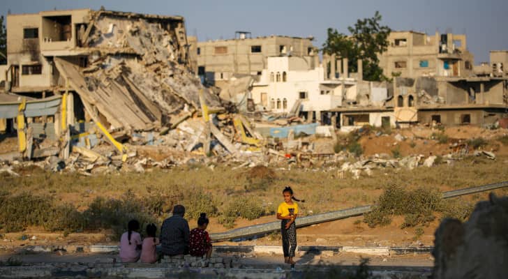 أشخاص يجلسون بالقرب من أنقاض المباني التي دمرت خلال قصف الاحتلال على مخيم المغازي للاجئين الفلسطينيين
