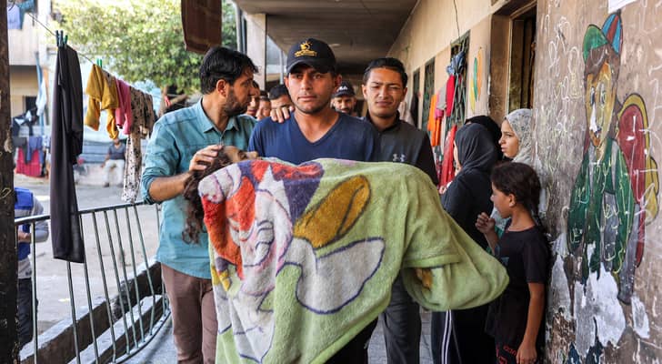 فلسطيني يحمل جثمان فتاة استشهدت في قصف على مدرسة الرافعي بمخيم جباليا