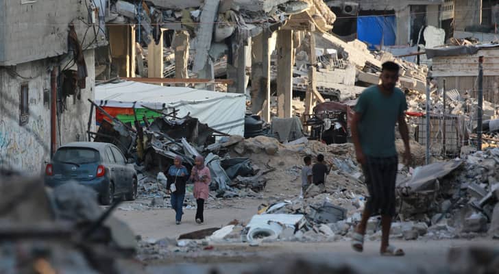فلسطينيون يمرون بجوار مبان مدمرة في خان يونس جنوب قطاع غزة