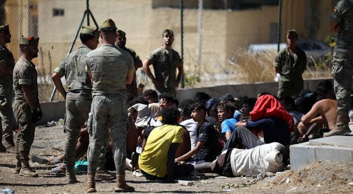 جنود مشاة إسبان يراقبون مجموعة من المهاجرين يجلسون على الأرض في جيب سبتة الإسباني